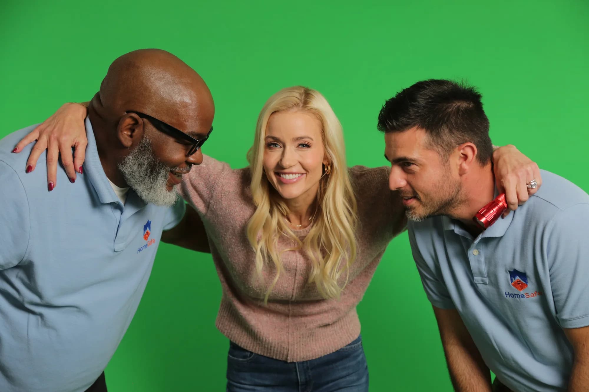 Three performers smiling together in front of a green screen