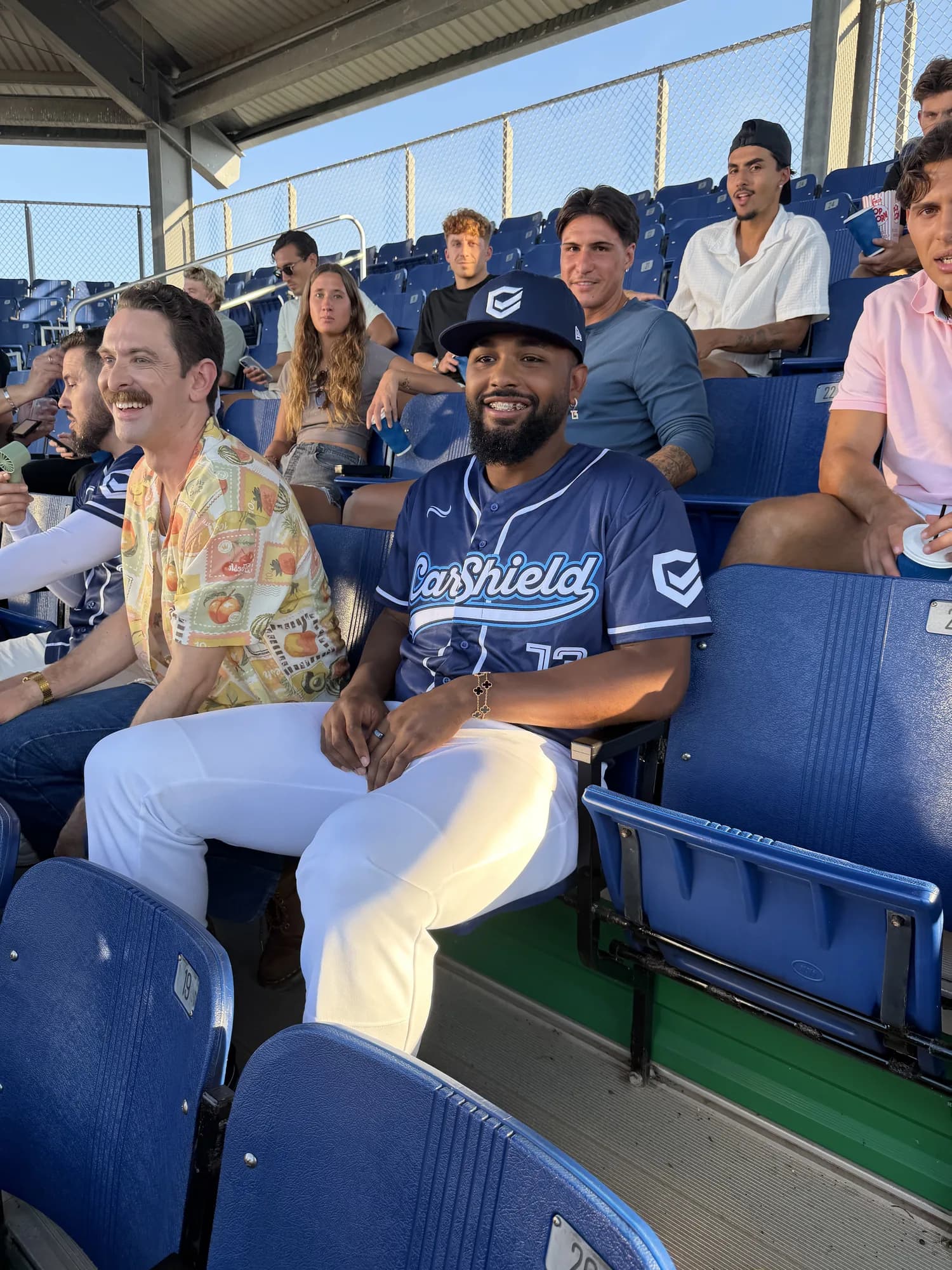 A performer in a CarShield jersey seated among spectators in stadium seats
