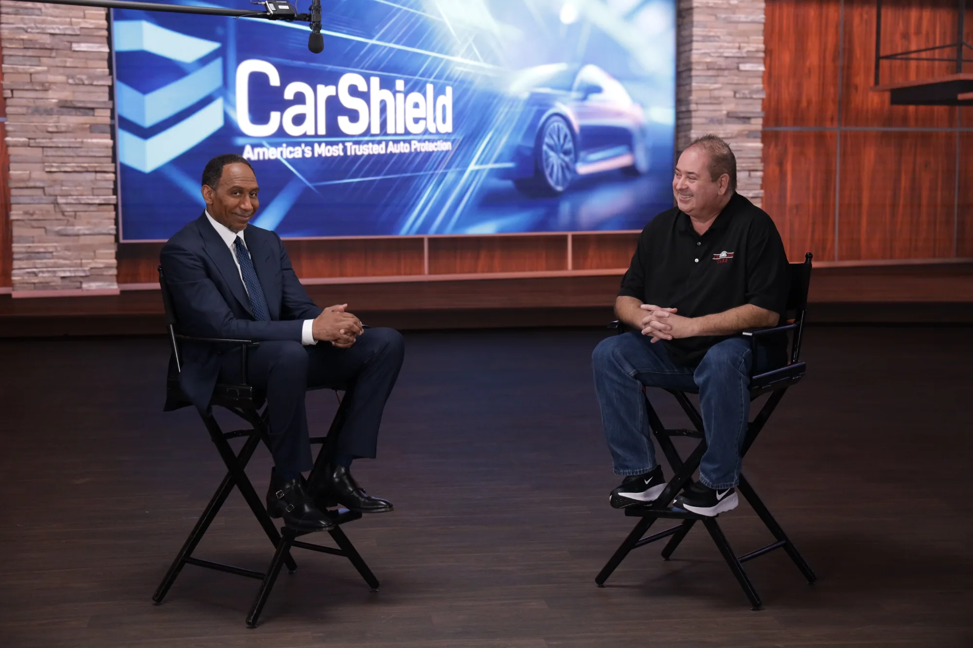Two on-camera performers seated in front of a CarShield screen